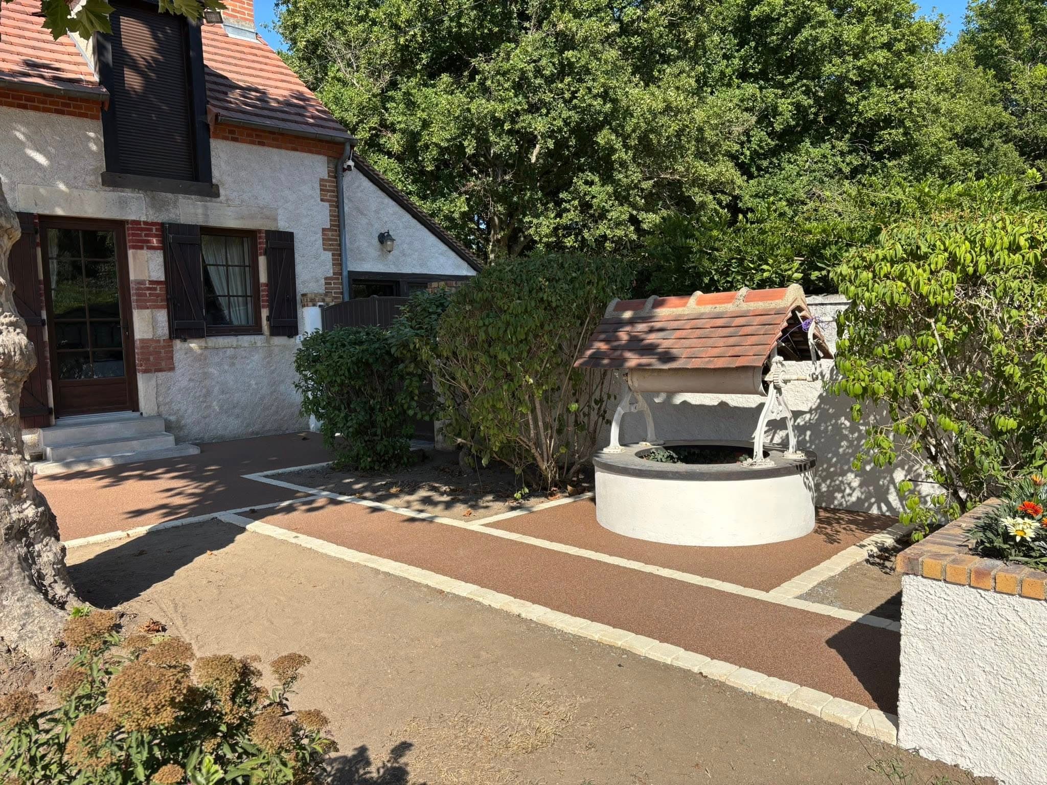 Terrasse en tapis de pierre ton terracotta autour d’un puits